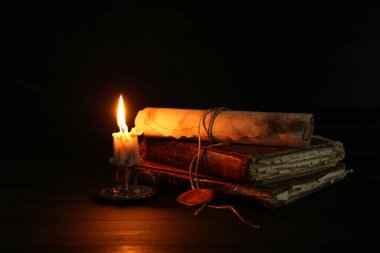 Eski parşömen, yanan mum ve siyah ahşap masa üzerindeki kitaplar, yakın plan.