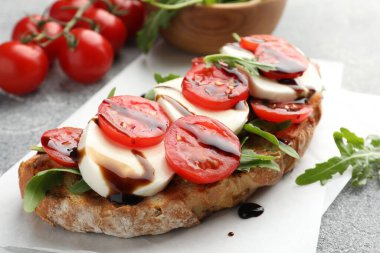 Mozarella peynirli lezzetli sandviç, balzamik sos, domates ve roka gri masada, yakın plan.