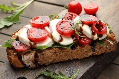 Mozarella peynirli lezzetli sandviç, balzamik sos, domates ve roka ahşap masada, yakın plan.