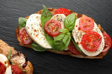 Mozarella peynirli, domatesli ve fesleğenli lezzetli sandviçler siyah masada, düz yerde.