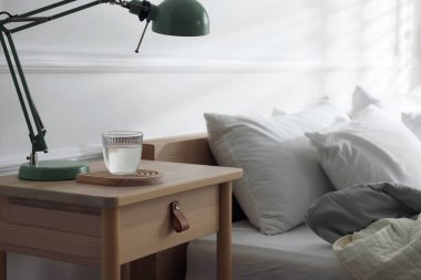 Yatak odasının yanında lamba ve bir bardak su olan komodinin yanında.