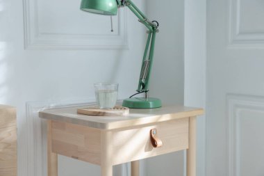 İçinde lamba ve bir bardak su olan komodinin yanında.