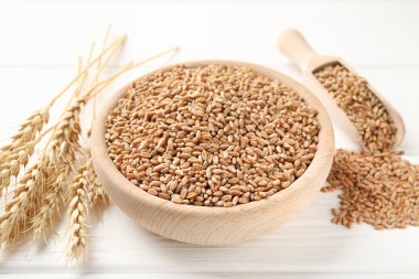 Kasede buğday taneleri, beyaz ahşap masada kepçe ve çiviler, yakın plan.