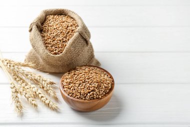 Kase içinde buğday taneleri, çuval bezi torbası ve beyaz tahta masa üzerinde çivili çubuklar, metin için yer