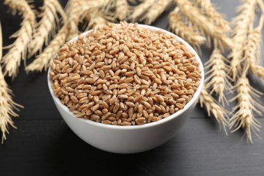 Kasede buğday taneleri ve siyah ahşap masada çiviler, yakın plan.