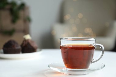 Bulanık ışıklara karşı beyaz masanın üzerinde bir fincan çay ve kek.