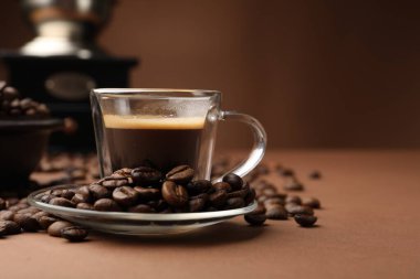 Kahverengi arka planda bir fincan sıcak kahve, öğütücü ve fasulye, yakın plan. Metin için boşluk