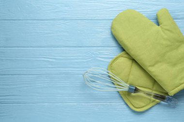 Yeşil fırın eldiveni, tutkal ve açık mavi ahşap masa üzerinde çırpma, düz uzanma. Metin için boşluk