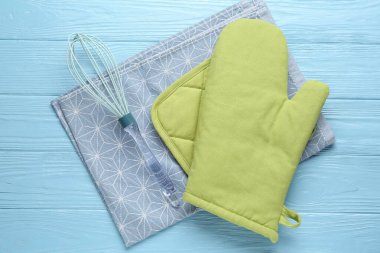 Yeşil fırın eldiveni, tutucu, havlu ve çırpıcı açık mavi ahşap masa, düz uzanma