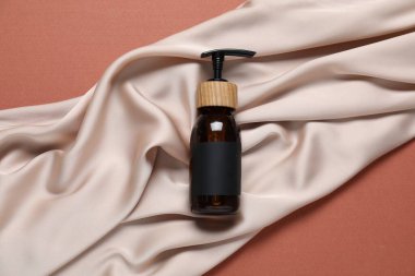 Kahverengi arka planda kozmetik ürün ve kumaş, üst görünüm. Tasarım için model