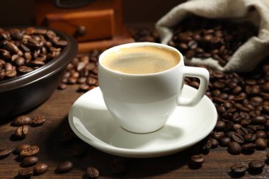 Aromatik kahve fincanda ve fasulyeler ahşap masada, yakın plan.