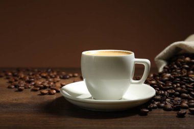 Kahverengi arka planda kahve fincanı ve ahşap masada fasulye, yakın plan.