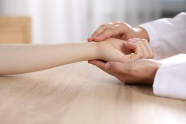 Doktor kadının nabzını kontrol ediyor. Ahşap masada parmaklarıyla, yakın plan.