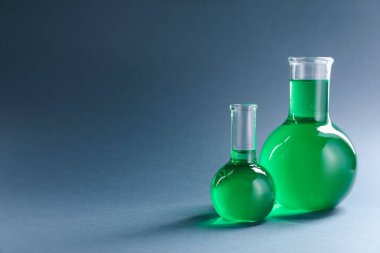 Gri zemin üzerinde yeşil sıvı bulunan laboratuvar camları. Metin için boşluk