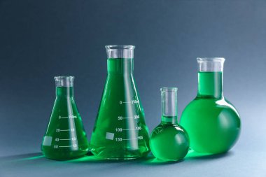 Gri zemin üzerinde yeşil sıvı bulunan laboratuvar camları.