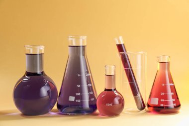 Bej arka planda renkli sıvılar bulunan laboratuvar camları.