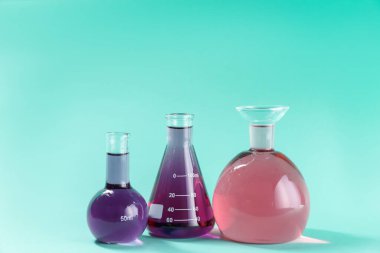 Turkuaz arka planda renkli sıvılar bulunan laboratuvar camları. Metin için boşluk