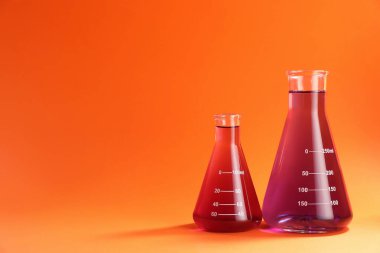 Turuncu zemin üzerinde kırmızı sıvı bulunan laboratuvar camları. Metin için boşluk
