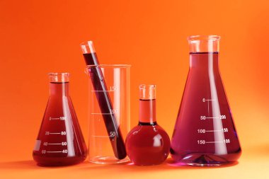 Turuncu zemin üzerinde kırmızı sıvı bulunan laboratuvar camları.