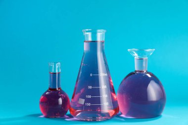 Açık mavi zemin üzerinde renk sıvısı bulunan laboratuvar camları