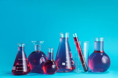 Açık mavi zemin üzerinde renk sıvısı bulunan laboratuvar camları. Metin için boşluk