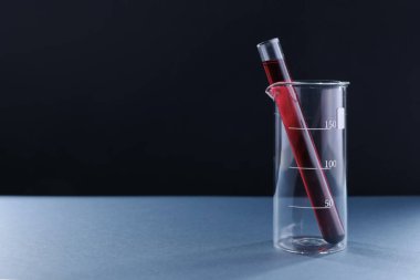 Siyah zemin üzerinde kırmızı sıvı bulunan laboratuvar camları. Metin için boşluk