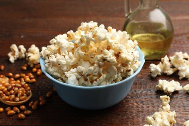 Lezzetli patlamış mısır, yağ ve mısır taneleri ahşap masada, yakın plan.