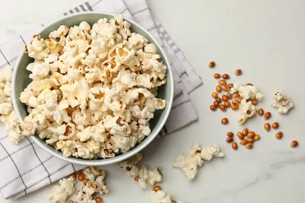 Lezzetli patlamış mısır ve mısır taneleri beyaz mermer masada, düz yerde.