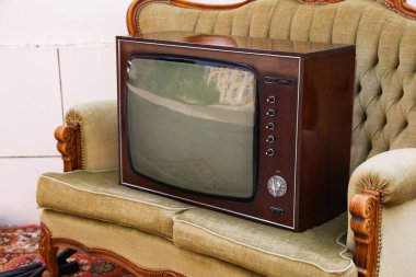 Dışarıdaki beyaz duvarın yanında kanepe ve halı üzerinde Retro TV. Kullanılmış eşyalar