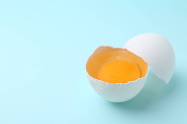 Açık mavi arka planda kırık bir tavuk yumurtası, yakın plan. Metin için boşluk