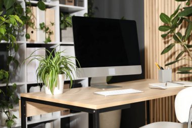 Modern bilgisayarı, kırtasiyesi ve çiçek dekoru olan şık bir iş yeri. Biyofilik iç tasarım