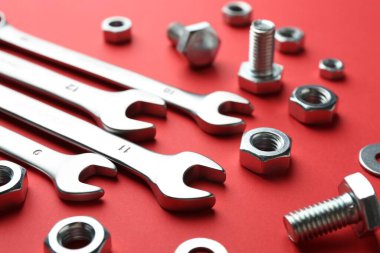 Kırmızı arkaplanda metal anahtarlar, somunlar ve cıvatalar, yakın plan.