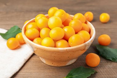 Olgun sarı kiraz erikleri ve yapraklar ahşap masada, yakın plan.