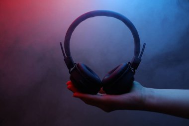 Karanlık arka planda kablosuz kulaklık tutan kadın. Renkli ışıklar ve duman, yakın plan.