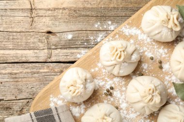 Biber, un ve defne yapraklarıyla ahşap masa üzerinde pişmemiş khinkaliler (hamur köfteleri). Metin için boşluk