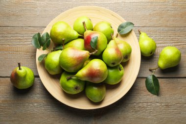 Taze armutlar ve ahşap masada yeşil yapraklar, düz uzanmış.