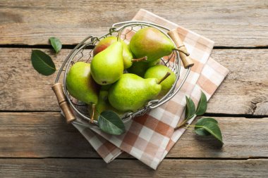Metal sepetin içinde taze armutlar ve ahşap masanın üzerinde yeşil yapraklar.