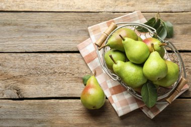 Metal sepetin içinde taze armutlar ve ahşap masanın üzerinde yeşil yapraklar. Metin için boşluk