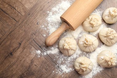 Ahşap masa üzerinde merdane ve un ile pişirilmemiş khinkaliler (hamur tatlısı) düz yatıyordu. Metin için boşluk