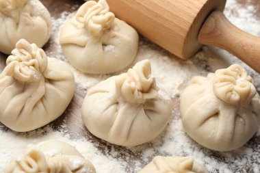 Ahşap masa üzerinde merdane ve un ile pişirilmemiş khinkaliler (hamur tatlısı), yakın plan