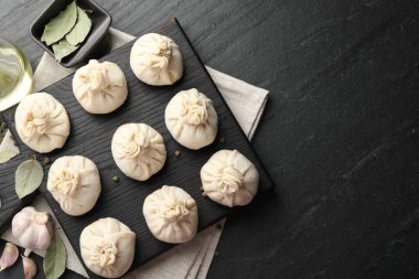 Biber, sarımsak ve defne yapraklarıyla pişirilmemiş khinkaliler (hamur köfteleri) siyah masada, düz yerde. Metin için boşluk