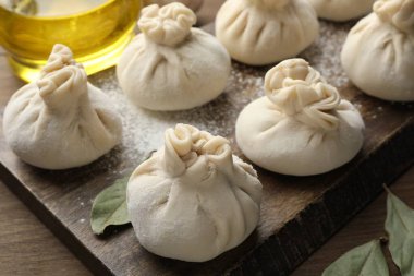 Ahşap masada un ve defne yapraklarıyla pişirilmemiş khinkaliler (hamur tatlısı), yakın plan.