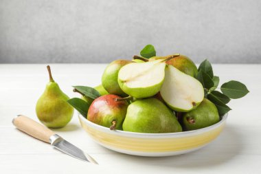 Taze armutlar, bıçak ve yeşil yapraklar beyaz ahşap masada, yakın plan.
