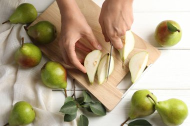 Beyaz ahşap masada taze olgun armut kesen bir kadın.