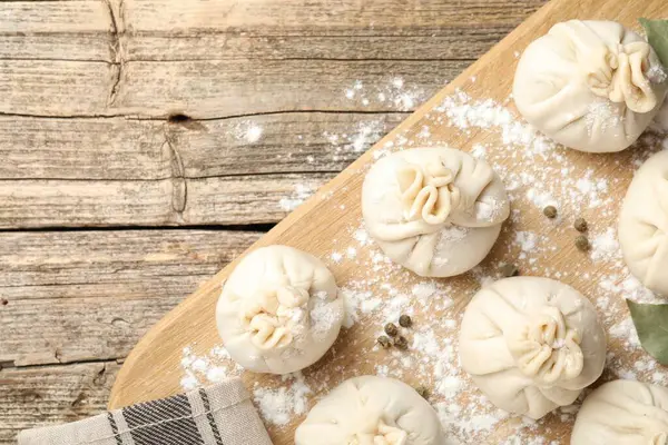 Biber, un ve defne yapraklarıyla ahşap masa üzerinde pişmemiş khinkaliler (hamur köfteleri). Metin için boşluk