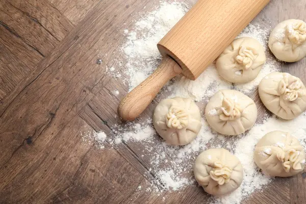 Ahşap masa üzerinde merdane ve un ile pişirilmemiş khinkaliler (hamur tatlısı) düz yatıyordu. Metin için boşluk