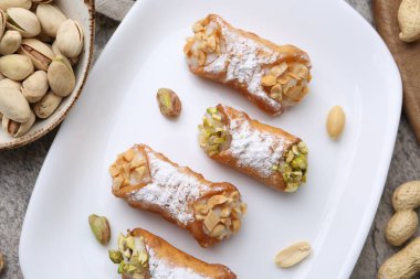 Ricotta peynirli, fıstıklı, şam fıstıklı ve pudra şekerli lezzetli cannoli gri desenli masa, düz uzanmış