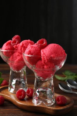 Tatlı kaselerinde nefis ahududu şerbeti, nane ve taze böğürtlen ahşap masada siyah arka planda, yakın planda.