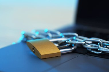 Siber güvenlik. Masada zincir ve dizüstü bilgisayarı olan metal asma kilit, yakın plan.