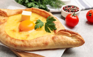 Peynirli, yumurtalı, maydanozlu ve açık gri arkaplanlı diğer ürünlerle lezzetli khachapuri, yakın plan.